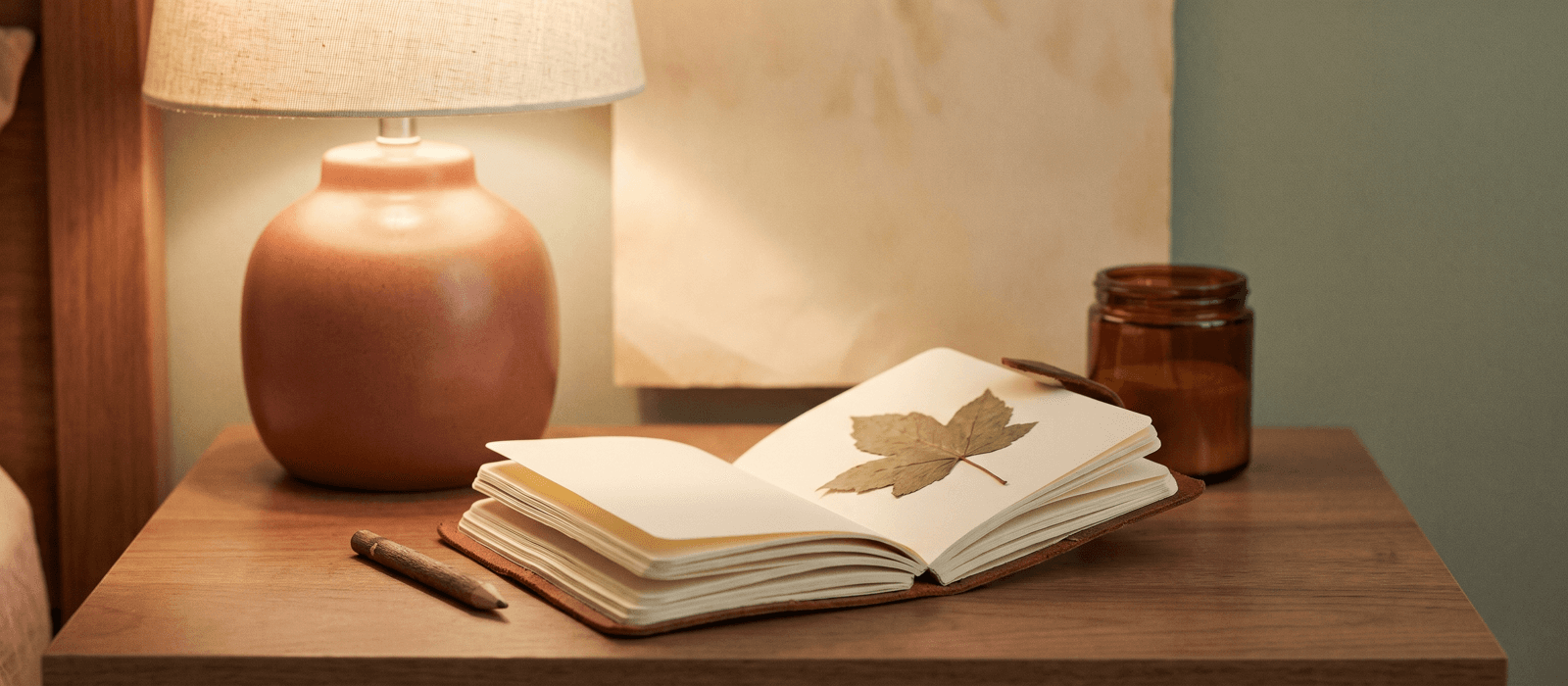 Pocket notebook with pencil and a pressed leaf in soft lamplight